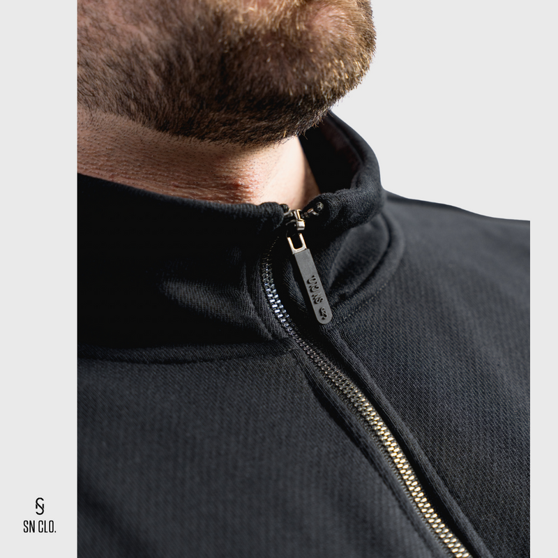 Close-up of a person wearing a black 3/4 zip sweatshirt with a rubber zipper, brand 'SN CLO.' visible.