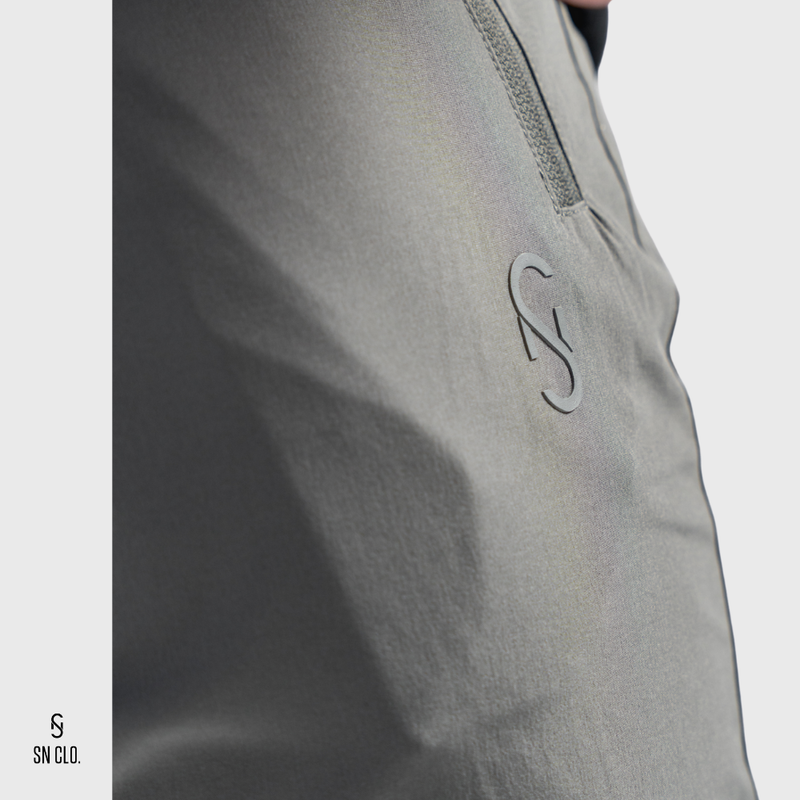 Close-up of a SN Clo. grey cargos with a zipper on the pocket and logo on a light grey background