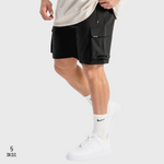 Man wearing black SN Clo cargo shorts and white sneakers on a light grey background