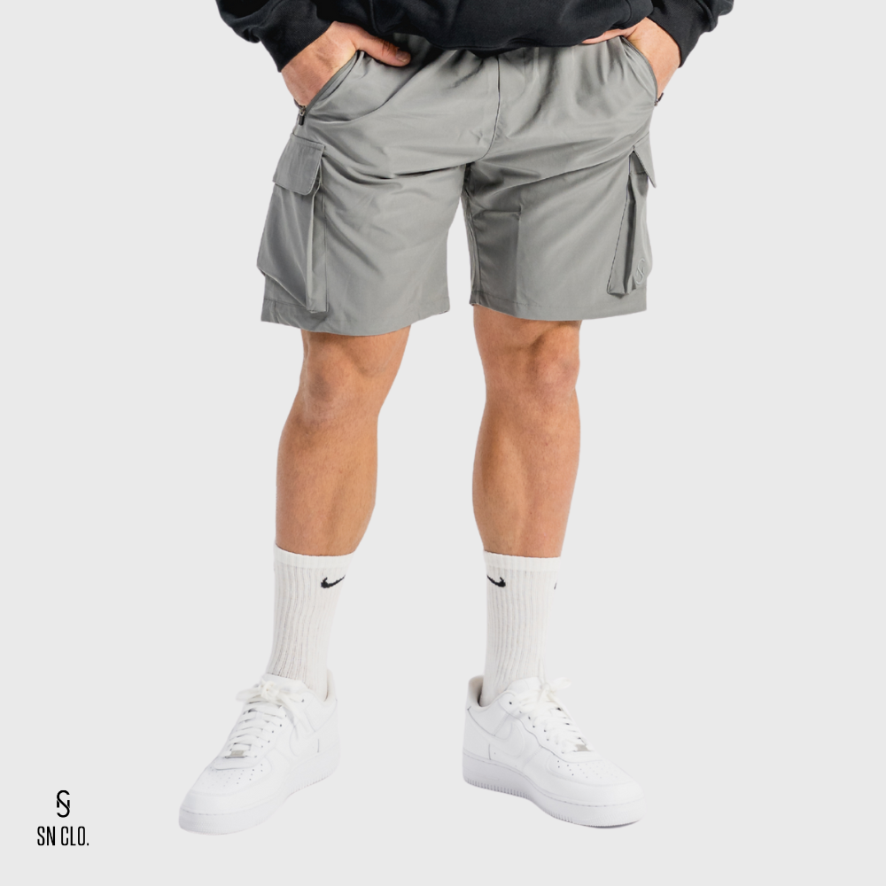 Man wearing grey SN Clo cargo shorts and white sneakers on a light grey background